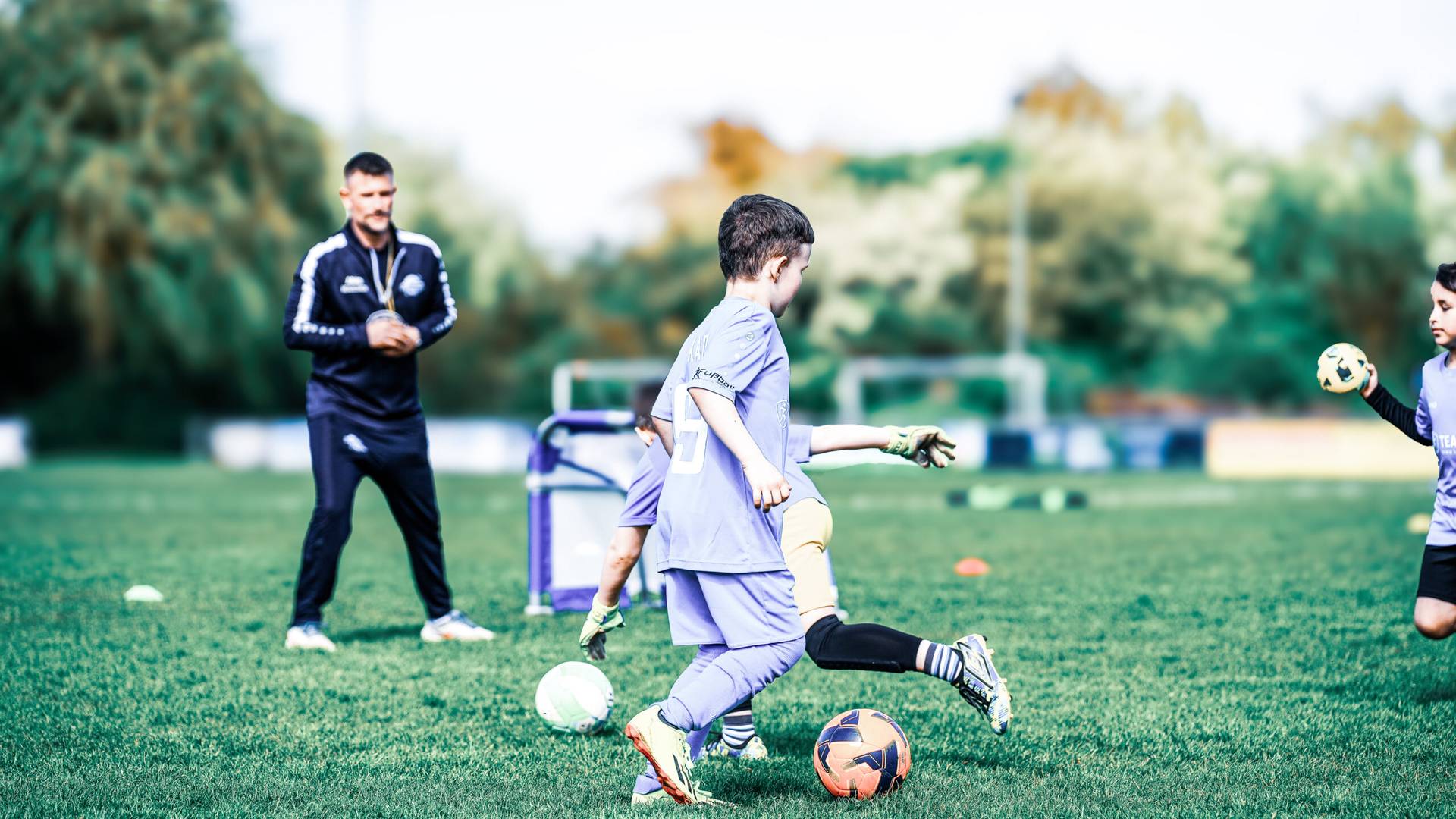 Ballschule: Kind dribbelt, der Trainer schaut zu