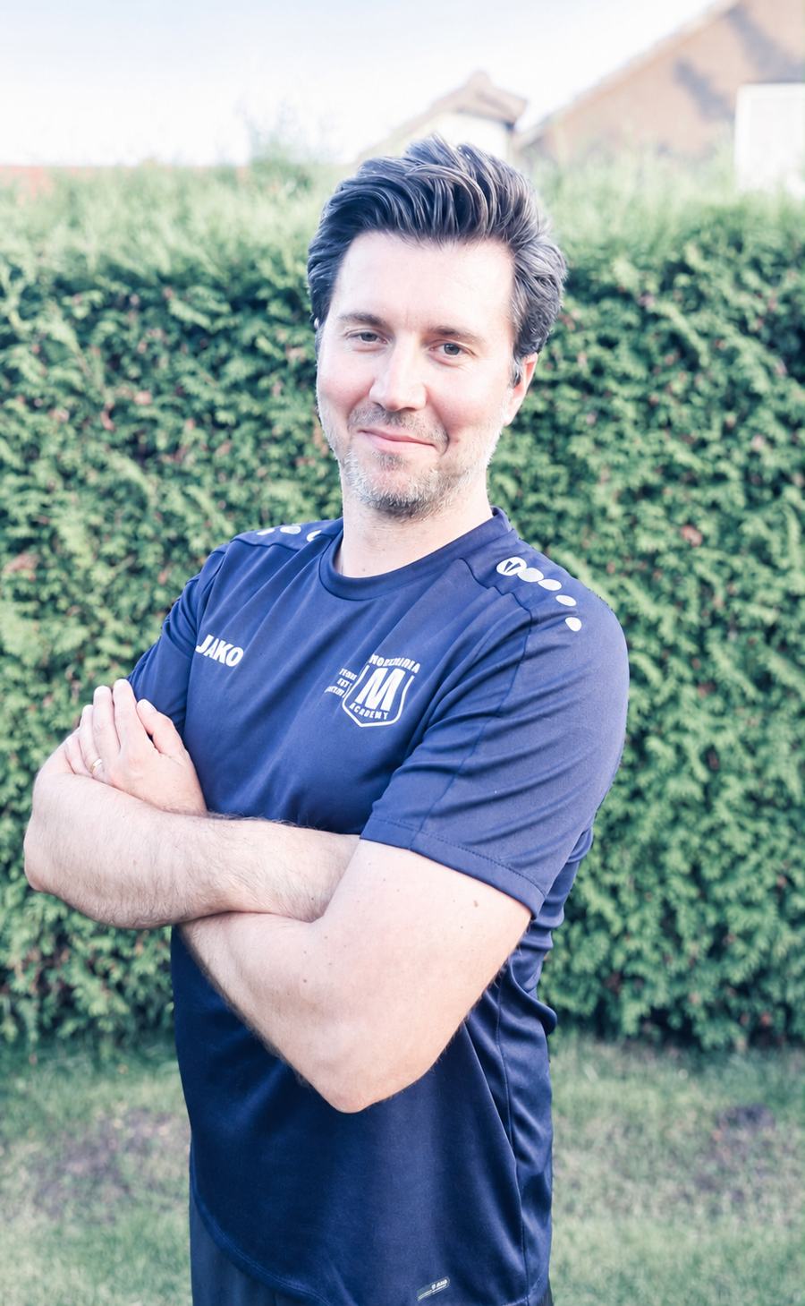 Martin Kazmierczak, Sportlicher Leiter, in Movemania-Trainingsshirt vor einer Hecke